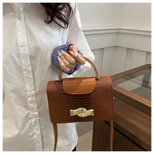 Close-up of brown crocodile texture leather bag with elegant gold metal wave clasp