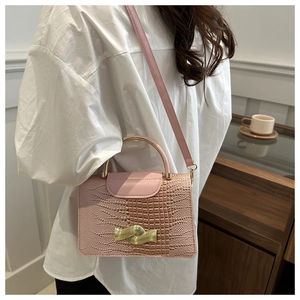 Detail of pink croc-embossed handbag with gold ring handle and metal wave clasp