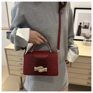 Detail showing red faux-croc texture with gold curved metal handle and stylish twist lock