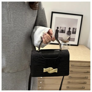 Detail view of black crocodile pattern handbag with golden wave buckle and curved handle
