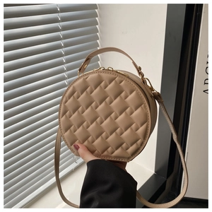 Detail of beige quilted round handbag featuring woven texture and gold hardware zipper