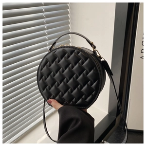 Macro shot of black quilted round handbag featuring elegant gold hardware and top handle