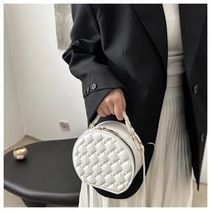 Detail of white quilted round crossbody bag with metal zipper and top handle on model