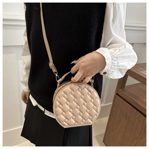 Detail of beige round crossbody bag featuring woven texture and light gold hardware accents