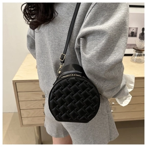 Detail of a black leather round crossbody bag with a woven texture shown on a model