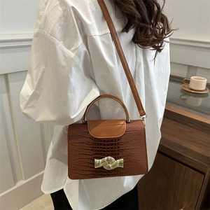 Brown crocodile embossed leather handbag with gold wave buckle shown on model