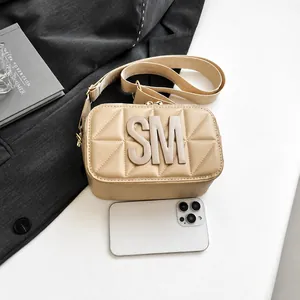 Detail van beige gewatteerde schoudertas met SM-logo en smartphone voor de maatreferentie