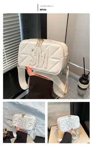 Detail van witte gewatteerde crossbodytas met gouden ritsen en SM-letterdecoratie op tas