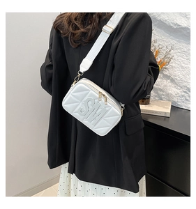 Detail van witte gewatteerde crossbodytas met gouden ritsen en reliëf SM-logo