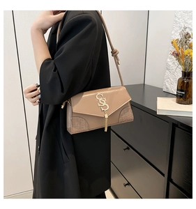 Detail of beige flap bag featuring gold double-S buckle, metal tassel, and croc-embossed trim