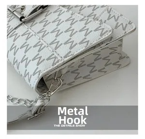 Dettaglio del gancio metallico argentato e della catena su una borsa bianca a motivi