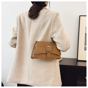 Dettaglio borsa monogramma marrone con catena d'argento indossata su un blazer beige