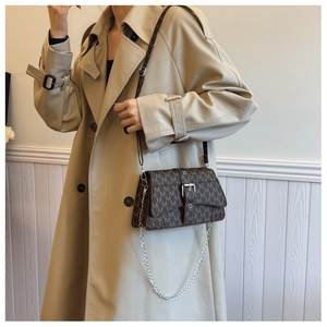 Dettaglio borsa marrone vintage con monogramma e fibbia argento su un trench coat