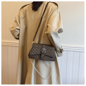 Borsa a tracolla marrone con monogramma e catena su un trench coat beige elegante