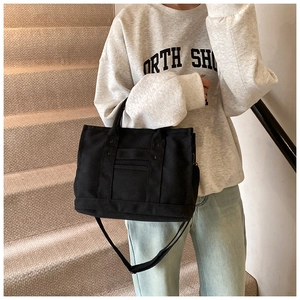 Detail of black canvas tote bag showing adjustable shoulder strap and functional pocket