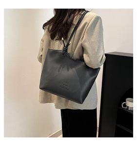 Detail of minimalist black tote bag featuring a knotted strap and fashion leather patch