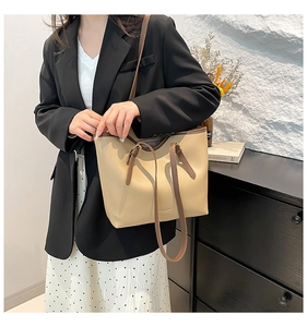 Detail of the adjustable brown leather strap and beige tote bag on a model's shoulder