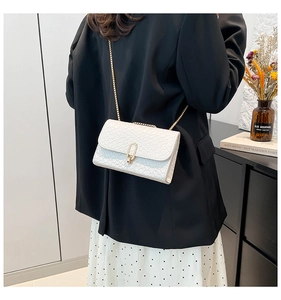 Detail of white embossed leather crossbody bag with elegant gold chain strap and buckle