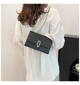Détail d'un sac bandoulière noir tissé avec serrure dorée et bandoulière chaîne sur modèle