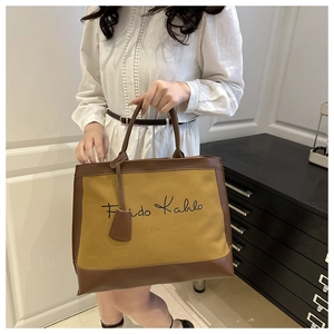 Detail of canvas tote bag with brown leather trim and Frida Kahlo script embroidery