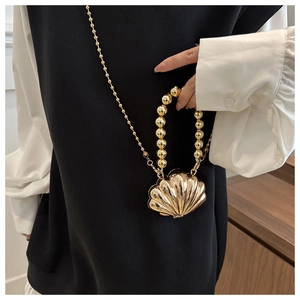 Polished gold shell-shaped mini bag with beaded handle and chain strap shown on person