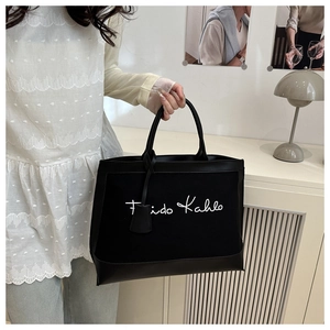 Detail view of large black canvas tote bag with Frida Kahlo script and leather charm