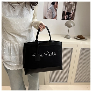 Detail view of canvas tote bag with Frida Kahlo print and black leather handles in cozy room