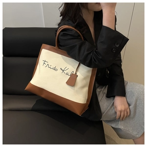 Detailed view of the large canvas tote bag with brown leather trim held by a model