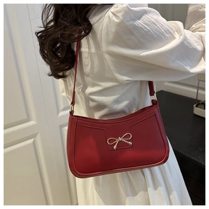 Détail du sac à bandoulière en cuir rouge avec nœud doré porté sur chemise blanche