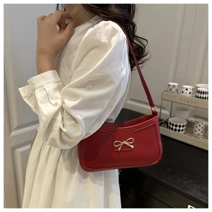 Détail du sac rouge en demi-lune avec nœud doré porté sur une robe en dentelle