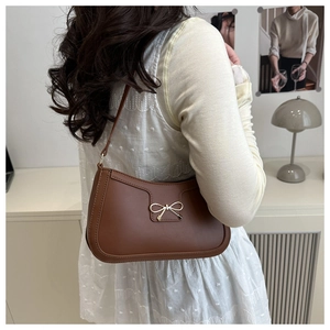 Gros plan d'un sac sous le bras marron avec boucle nœud dorée et design rétro incurvé