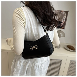 Détail du sac porté épaule noir avec boucle nœud doré sur un mannequin en intérieur