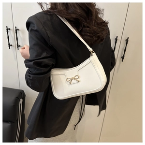 Petit sac blanc en cuir avec fermoir nœud doré porté à l'épaule dans un décor chic
