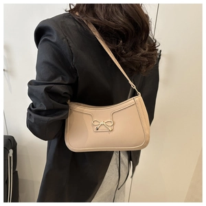 Vue latérale du sac hobo beige avec détail nœud doré porté sur un blazer noir