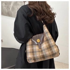 Detail of checkered woolen tote bag featuring a brown leather flap and gold 'N' metal buckle