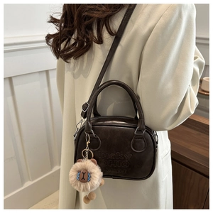 Detail der dunkelbraunen Retro-Ledertasche mit Gravur und Plüschlöwen-Anhänger