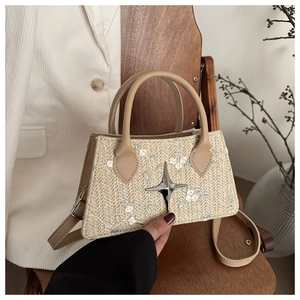 Detail of straw handbag with white flower embroidery and silver star buckle on wooden chair