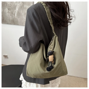 Detail of army green pleated tote bag with a small plush sheep pendant on the side strap