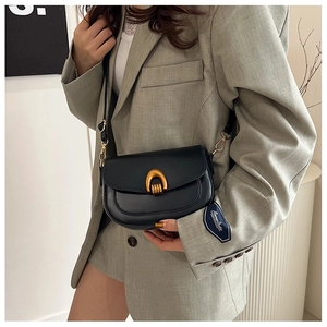 Detail of minimalist black saddle bag with vintage golden horseshoe buckle on grey blazer