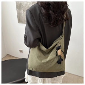 Detail of army green nylon pleated tote with brown sheep plush pendant on model