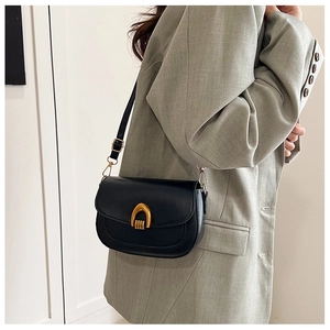 Black leather saddle bag featuring a gold arch buckle on a grey blazer model