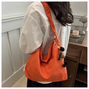 Detail of orange nylon pleated tote bag featuring a cute sheep plush charm on the shoulder strap