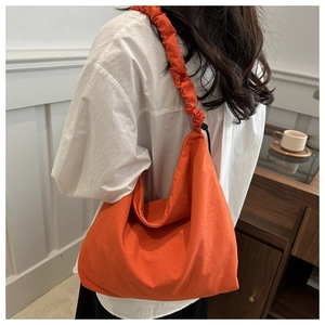 Detail of a bright orange crossbody bag with a trendy ruffled drawstring shoulder strap