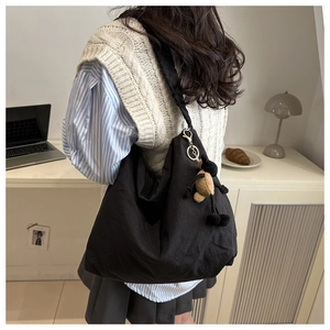 Detail of a black nylon drawstring tote bag featuring a cute plush bear charm accessory