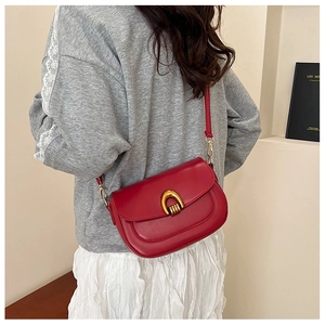Model wearing a red leather saddle bag with gold buckle and slim shoulder strap