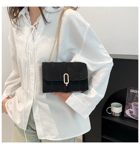 Detail of black crossbody bag with gold chain strap and oval metal buckle on fabric