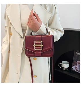 Detail of burgundy leather handbag with gold square buckle and cream trench coat styling