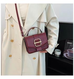 Chic burgundy leather crossbody bag with gold buckle worn on a stylish trench coat