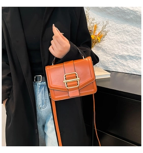 Detail of orange square handbag featuring a bold gold square lock and leather texture