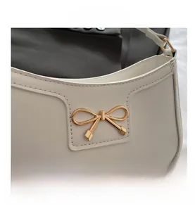 Close-up of golden bow hardware and fine stitching on a white leather crescent bag